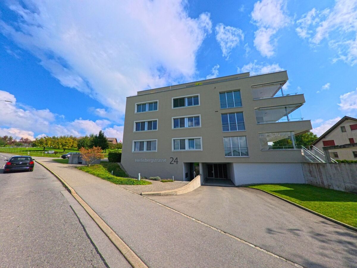 In Beromuenster (6215, Kanton Luzern) steht ein modernes Wohnhaus mit grossen Balkonen an einer leicht ansteigenden Strasse, die an Wiesen und Baumbestand vorbeifuehrt.