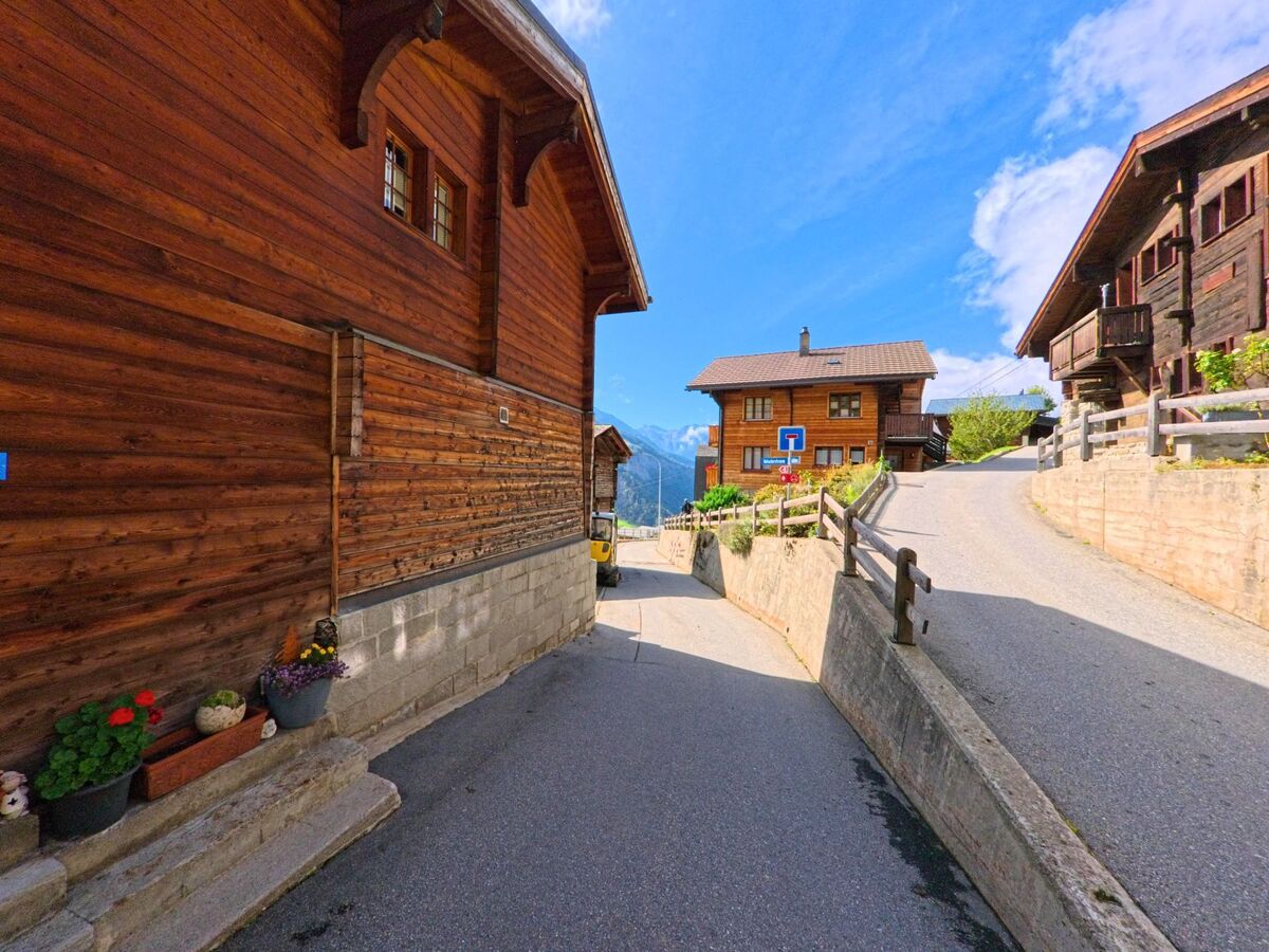 Zwischen traditionellen Holzhäusern in Bettmeralp (3991, Kanton Wallis) verläuft eine schmale Gasse mit Blick auf die Berge.