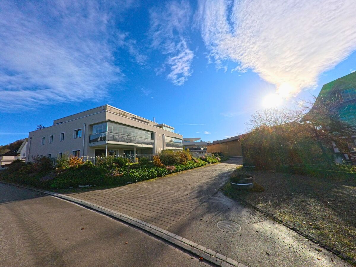 Am Rand eines Wohnquartiers in Bettwiesen (9553, Kanton Thurgau) führt ein gepflasterter Weg zu modernen Mehrfamilienhäusern mit begrünten Aussenflächen.