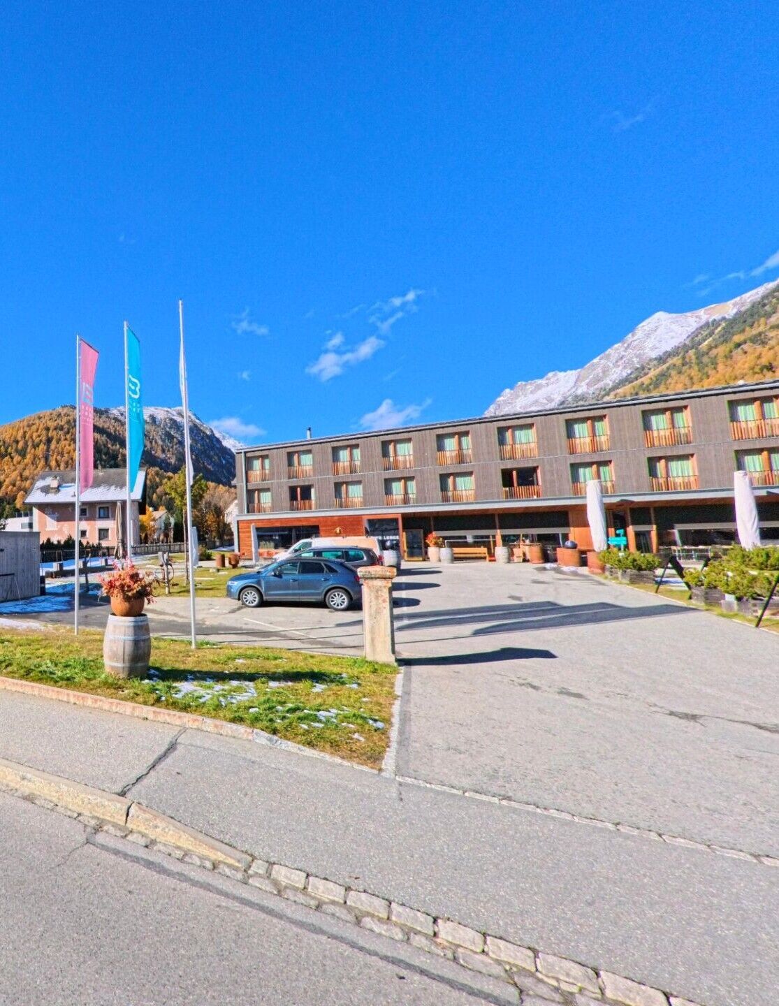 Vor einem grosszügigen Vorplatz mit Fahnenmasten zeigt sich in Bever (7502, Kanton Graubünden) ein langgestrecktes Gebäude, eingerahmt von alpiner Landschaft und herbstlichen Berghängen.