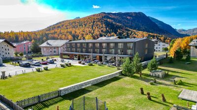 In Bever (7502, Kanton Graubuenden) befindet sich die Bever Lodge AG, ein modernes Hotelgebaeude mit grossem Gartenbereich und Blick auf bewaldete Berghaenge.