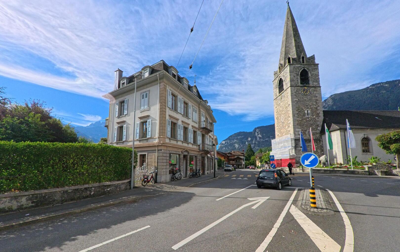 Am Rand der Altstadt von Bex (1880, Kanton Waadt) steht die Kirche mit ihrem markanten Steinturm neben einem historischen Wohnhaus.