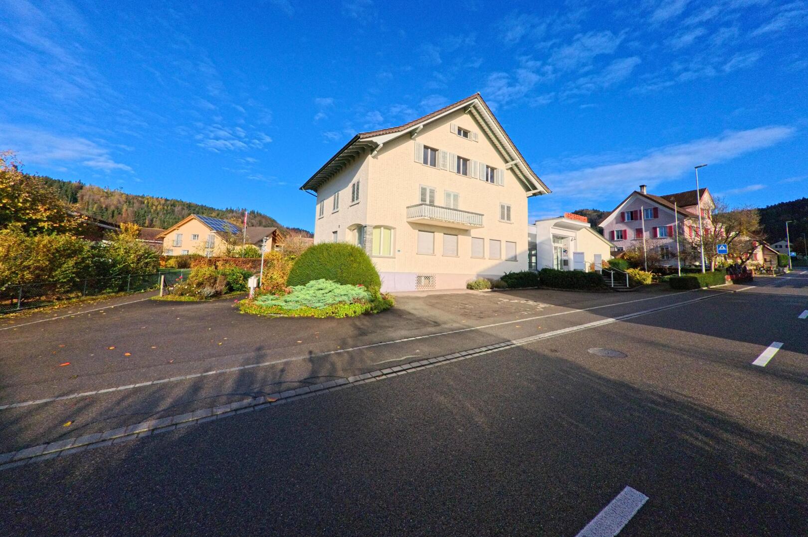 An einer ruhigen Strasse in Bichelsee-Balterswil (8362, Kanton Thurgau) steht ein helles Wohn- und Verwaltungsgebäude mit gepflegtem Vorgarten unter blauem Himmel.