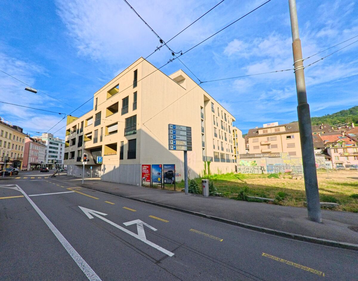 In Biel/Bienne (2500, Kanton Bern) zeigt sich ein modernes Wohngebäude an einer verkehrsreichen Strasse, während Strassenmarkierungen und Verkehrsschilder den urbanen Kontext unterstreichen.