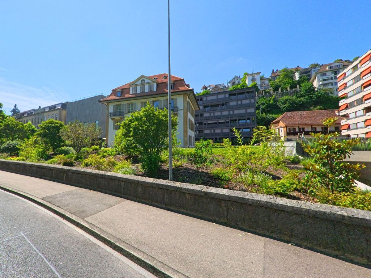 In Biel/Bienne (2500, Kanton Bern) zeigt sich eine malerische Strassenszene mit historischen und modernen Gebäuden, flankiert von grünen Flächen und einem hügeligen Hintergrund.