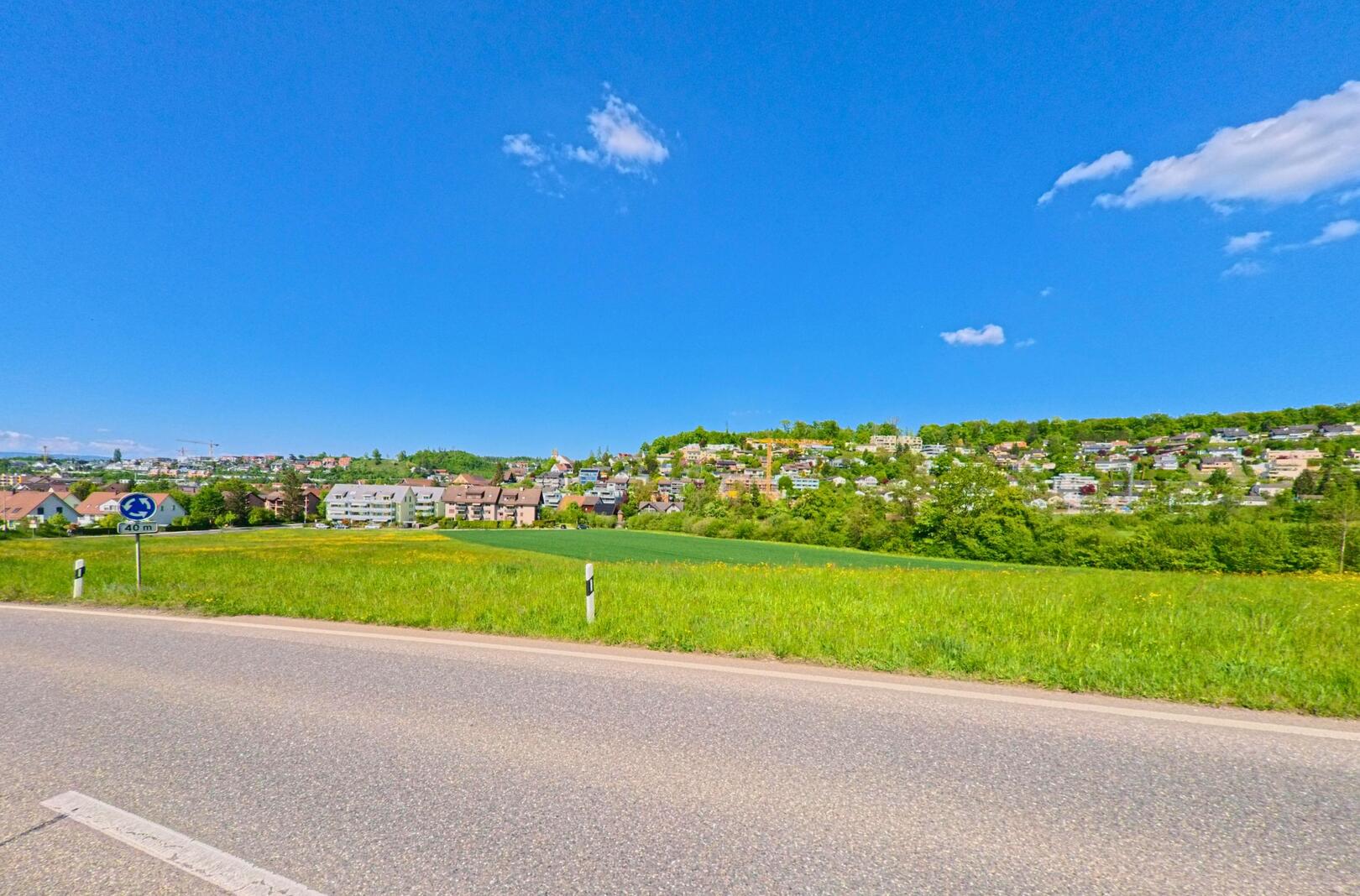 Von einer Landstrasse aus eröffnet sich in Birmensdorf, PLZ 8903 im Kanton Zürich, der Blick auf ein Wohnquartier mit dicht bebauten Hängen und grünem Umland.