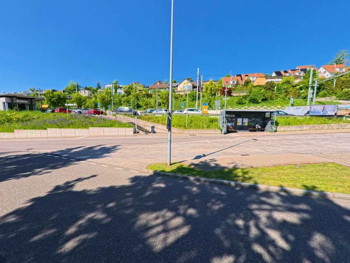 In Birmensdorf, PLZ 8903 im Kanton Zürich, liegt eine Bushaltestelle unterhalb eines mit Wohnhäusern bebauten Hügels, mit Parkplätzen und Bahngeleisen im Hintergrund.