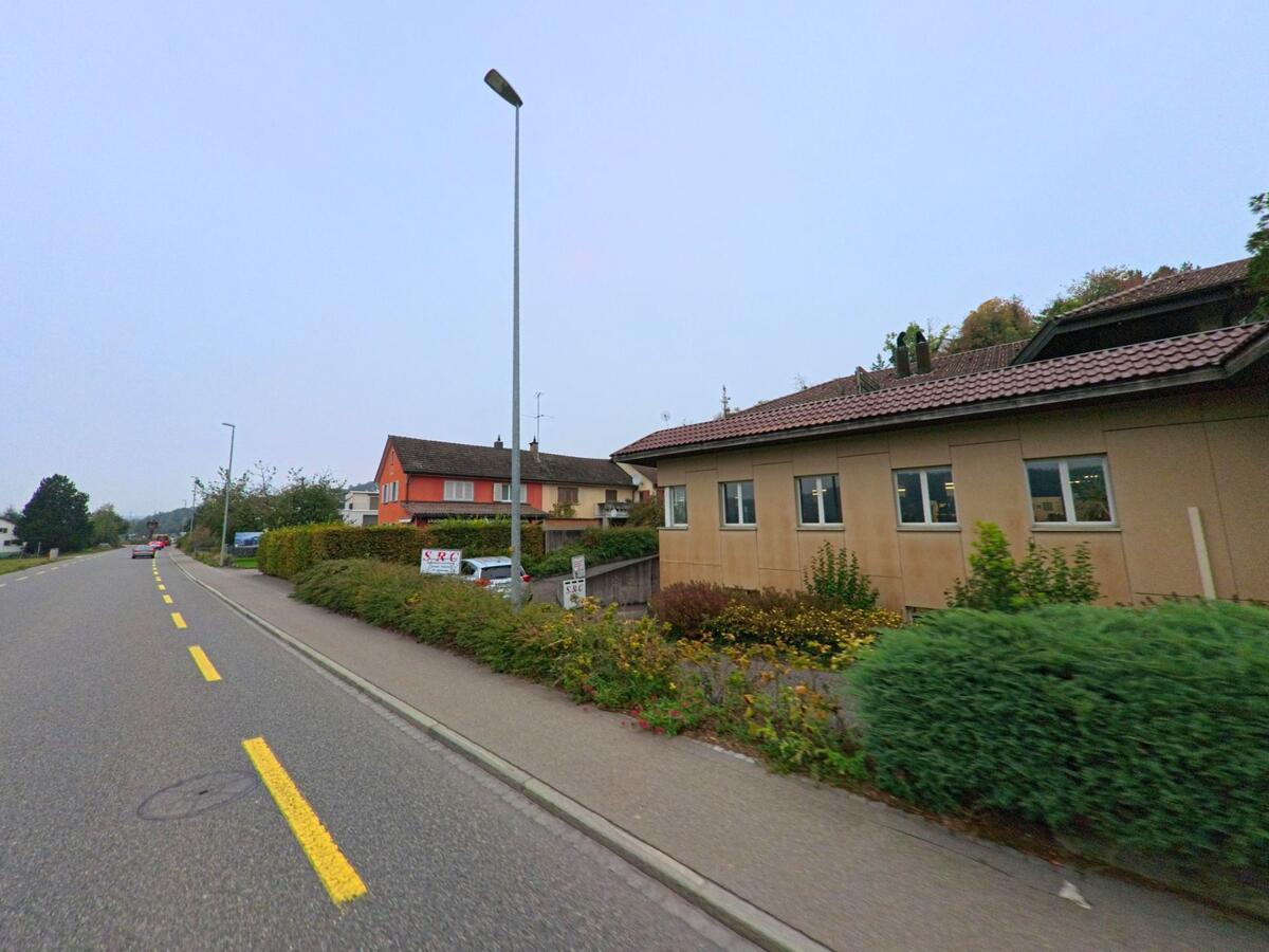 Entlang der Hauptstrasse in Birmenstorf (5413, Kanton Aargau) reihen sich Wohnhaeuser und kleine Betriebe mit gepflegten Vorgartenanlagen.