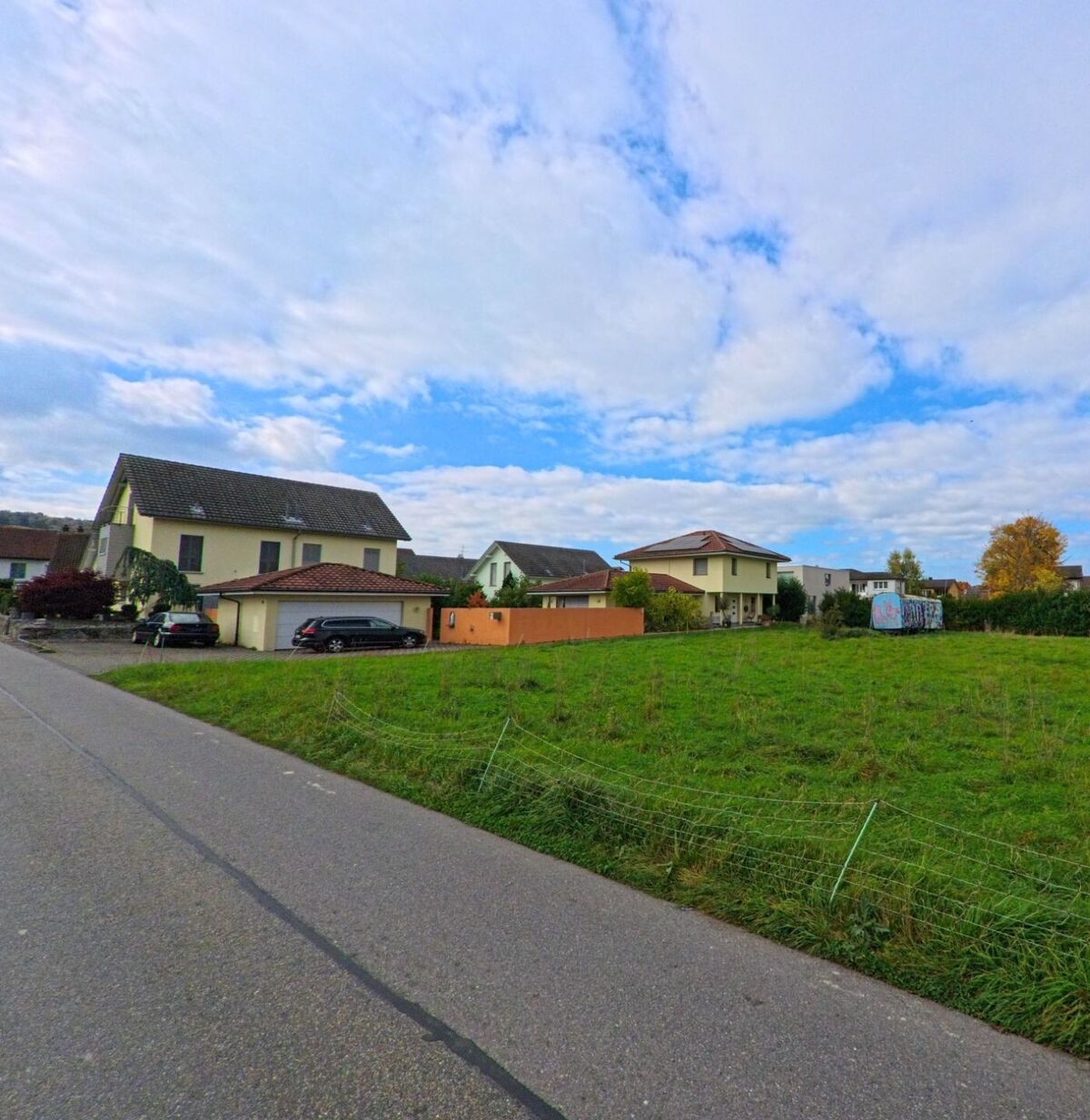 Am Ortsrand von Birr (5242, Kanton Aargau) stehen moderne Einfamilienhaeuser mit Gaerten entlang einer schmalen Strasse und angrenzender Wiese.