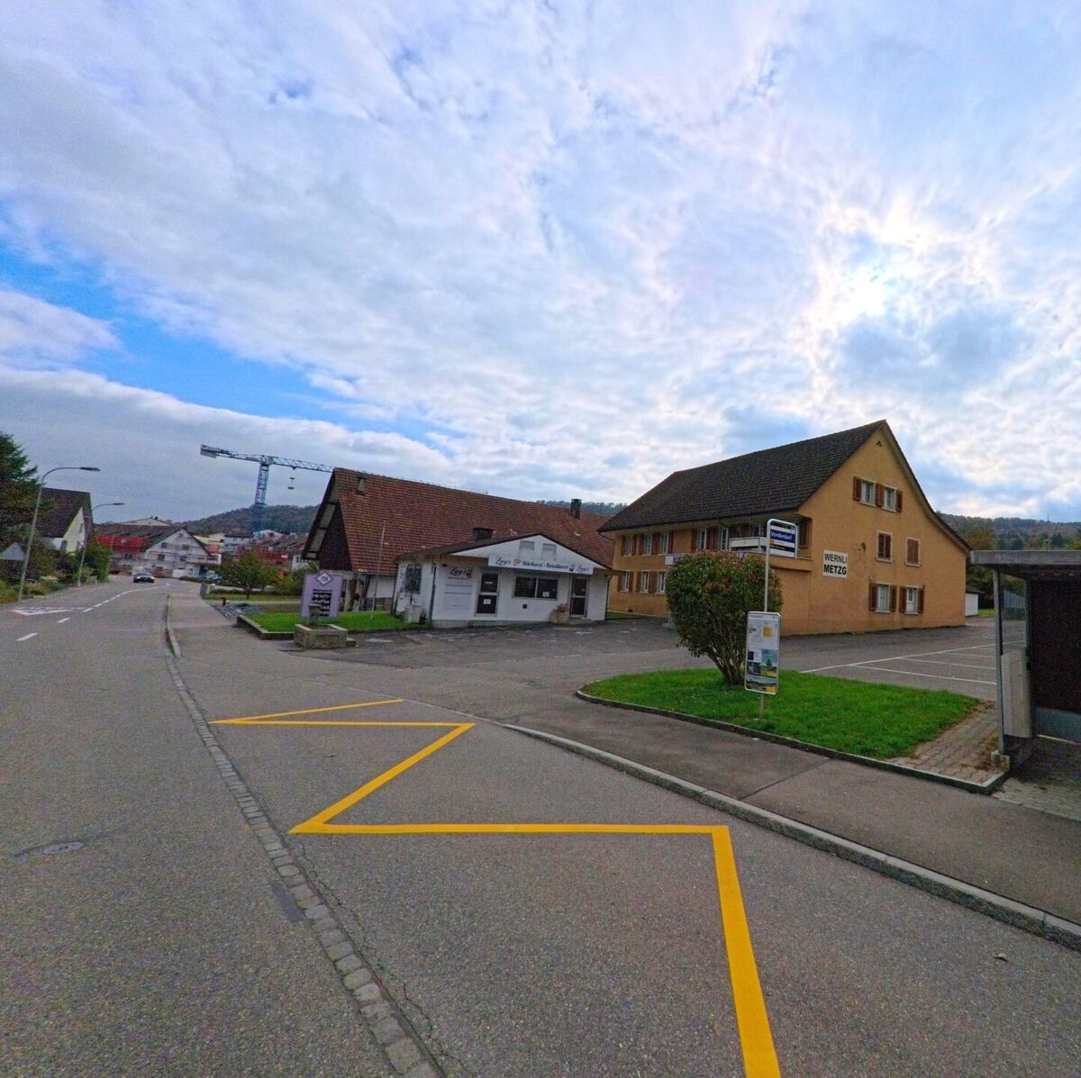 An der Hauptstrasse in Birr (5242, Kanton Aargau) befinden sich ein traditionsreiches Gebaeude mit Metzgerei und weitere Gewerbebauten vor bewaldetem Hintergrund.