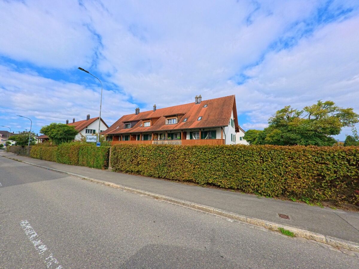Am Ortsrand von Birr (5242, Kanton Aargau) stehen Reihenhaeuser mit roten Daechern und gepflegten Hecken entlang einer ruhigen Strasse.