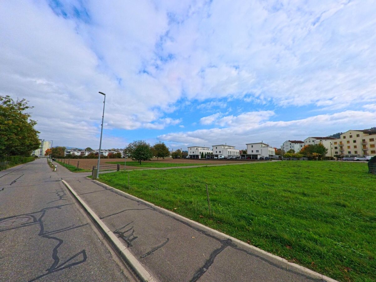 Offene Felder und moderne Wohnhaeuser praegen das Landschaftsbild am Siedlungsrand von Birr (5242, Kanton Aargau) unter einem teils bewölkten Himmel.