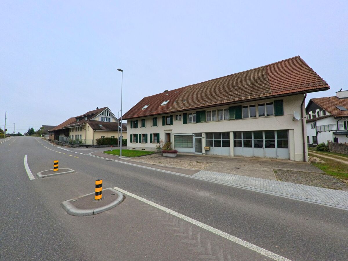 An der Hauptstrasse von Birrhard (5244, Kanton Aargau) stehen traditionelle Wohnhäuser mit roten Ziegeldächern und grünen Fensterläden.