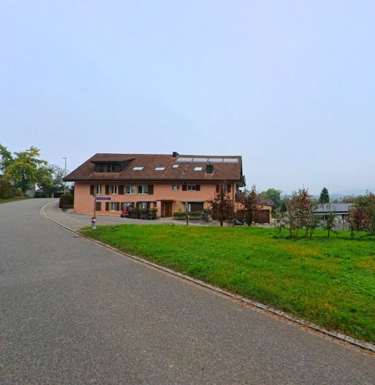 Am Hang in Birrhard (5244, Kanton Aargau) steht ein rosafarbenes Wohnhaus mit Solarpanels auf dem Dach und Blick über die umliegenden Felder.
