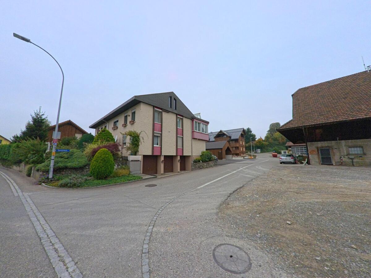 An einer Kreuzung in Birrhard (5244, Kanton Aargau) stehen Wohnhäuser und Bauerngebäude, umgeben von gepflegten Gärten und ruhigen Strassen.