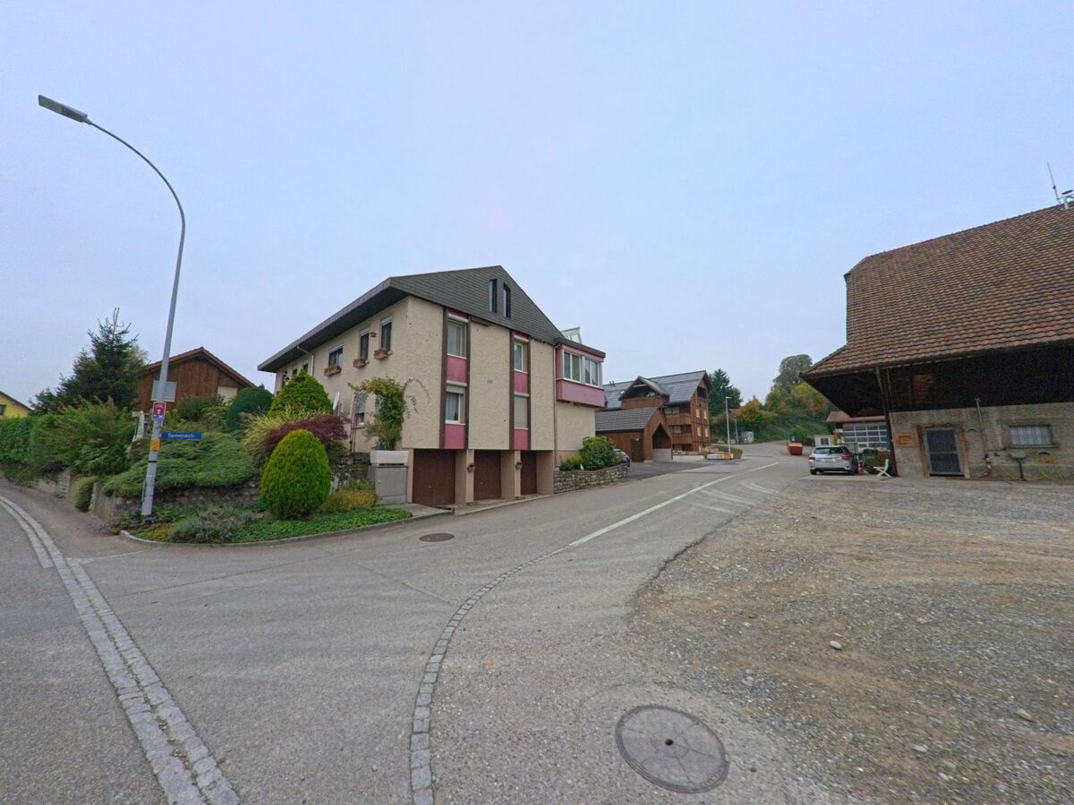 An einer Kreuzung in Birrhard (5244, Kanton Aargau) stehen Wohnhäuser und Bauerngebäude, umgeben von gepflegten Gärten und ruhigen Strassen.