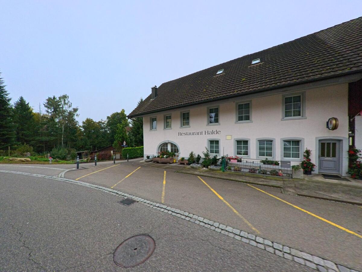 Das Restaurant Halde in Birrhard (5244, Kanton Aargau) liegt an einer ruhigen Strasse und ist von Bäumen und gepflegten Beeten umgeben.