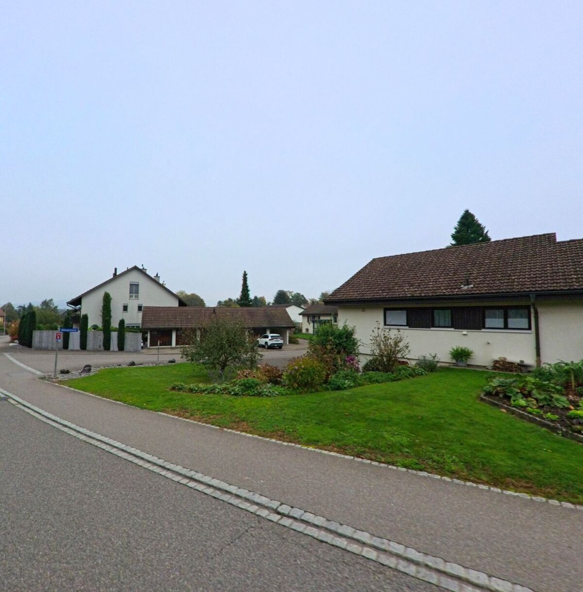 In einem Wohnquartier von Birrhard (5244, Kanton Aargau) stehen Einfamilienhäuser mit gepflegten Vorgärten an einer leicht gebogenen Strasse.