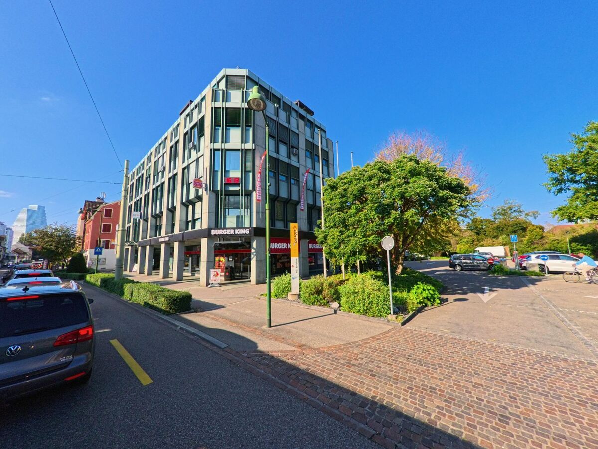 Nahe der Grenze zu Basel zeigt sich in Birsfelden (4127, Kanton Basel-Landschaft) ein modernes Eckgebaeude mit Gastronomie im Erdgeschoss und dichter Umgebungsbebauung.