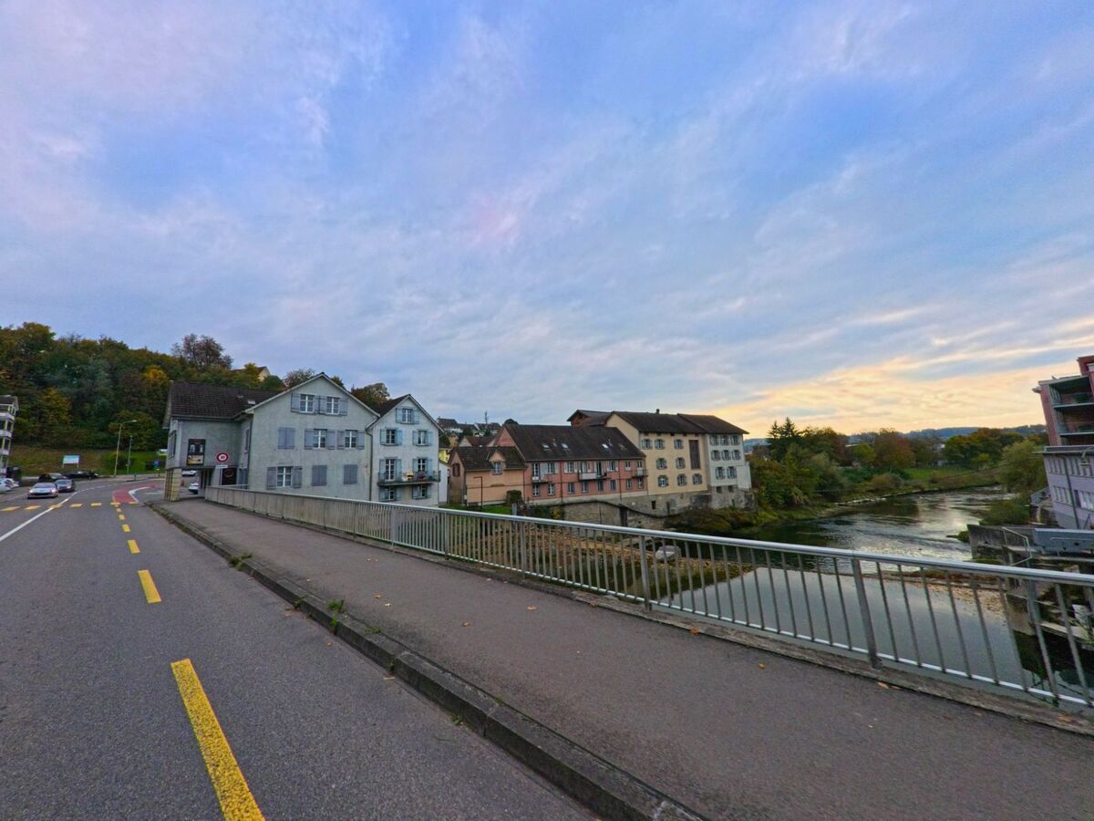 Entlang einer Bruecke in Bischofszell (9220, Kanton Thurgau) verläuft ein Gehweg mit Blick auf den Fluss und eine Reihe historischer Wohnhaeuser am Ufer.