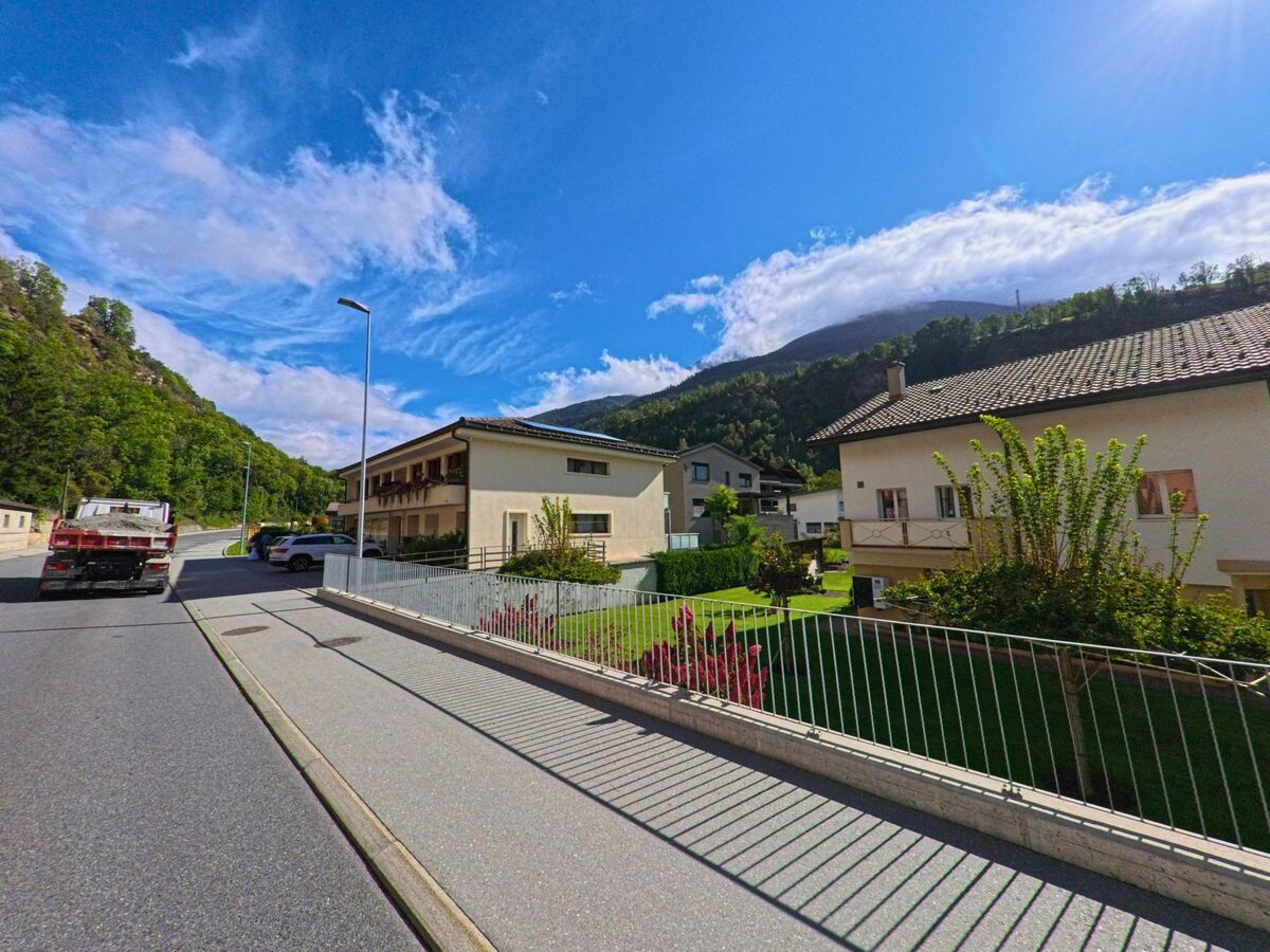 Einfamilienhaeuser mit gepflegten Gaerten in Bitsch (3982, Kanton Wallis) liegen an einer ruhigen Strasse mit Blick auf die bewaldeten Berge.