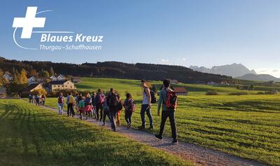 Auf einem Feldweg in Weinfelden (8570, Kanton Thurgau) wandert eine Gruppe von Menschen bei Abendlicht durch die offene Landschaft.