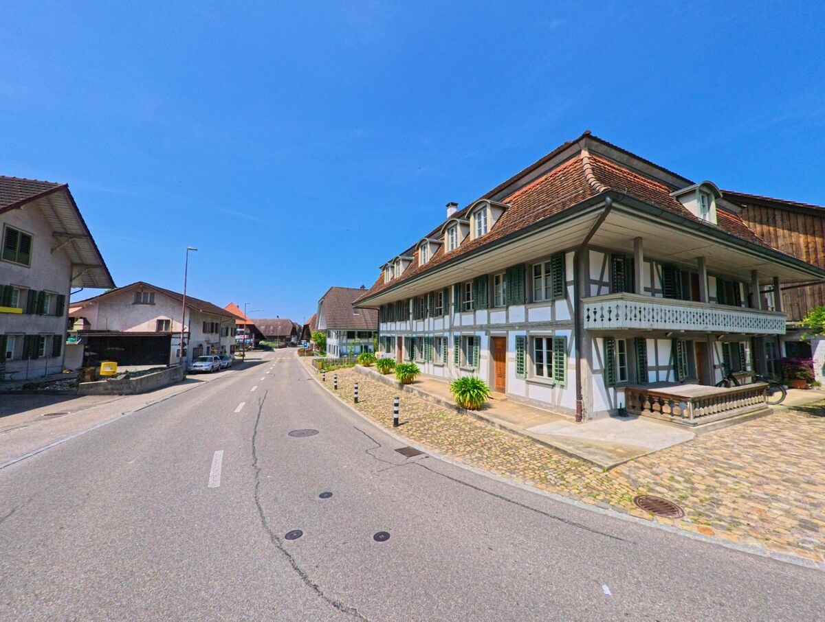 Ein gepflegtes Riegelhaus mit grünen Fensterläden steht in Bleienbach (3368, Kanton Bern) an einer leicht geschwungenen Strasse mit Kopfsteinpflaster und ländlichem Charme.