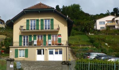 In Grandson (1422, Kanton Waadt) steht das BnB Tuileries, ein helles Haus mit gruenen Fensterlaeden und Balkonen, umgeben von Gaerten und Hanggelaende.