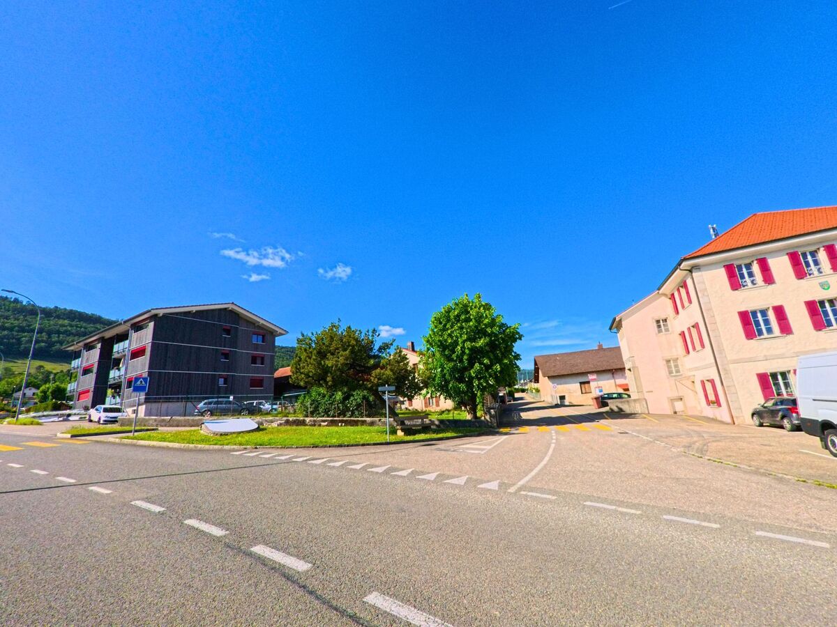 In Boécourt (2856, Kanton Jura) sind moderne und traditionelle Gebäude entlang einer Straße zu sehen, mit einer grünen Landschaft im Hintergrund.