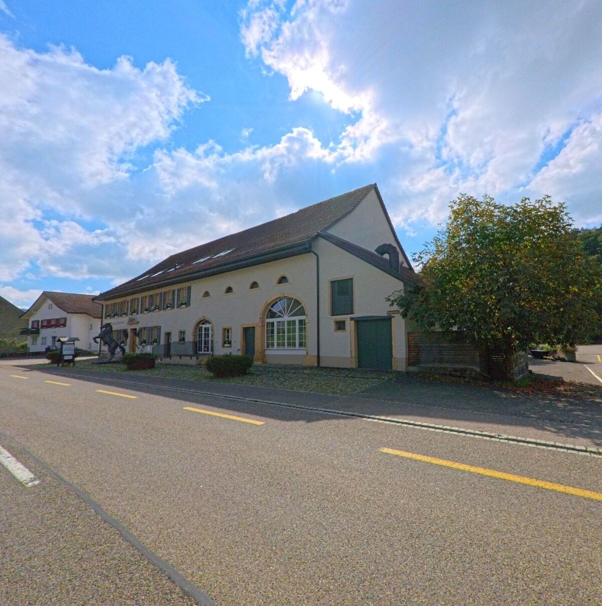 Ein helles Gebäude mit grossen Fenstern und gepflegter Fassade steht an der Hauptstrasse von Böztal (5077, Kanton Aargau), im Vordergrund führt die Strasse leicht bergauf.