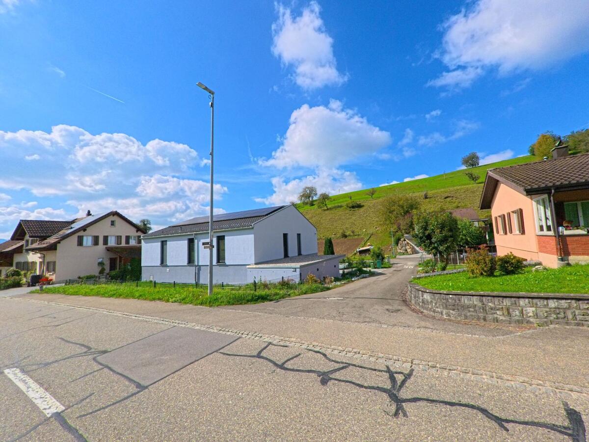 Am Hang von Böztal (5077, Kanton Aargau) liegen moderne und traditionelle Wohnhäuser an einer ruhigen Strasse mit Blick auf grüne Wiesen und Obstbäume.