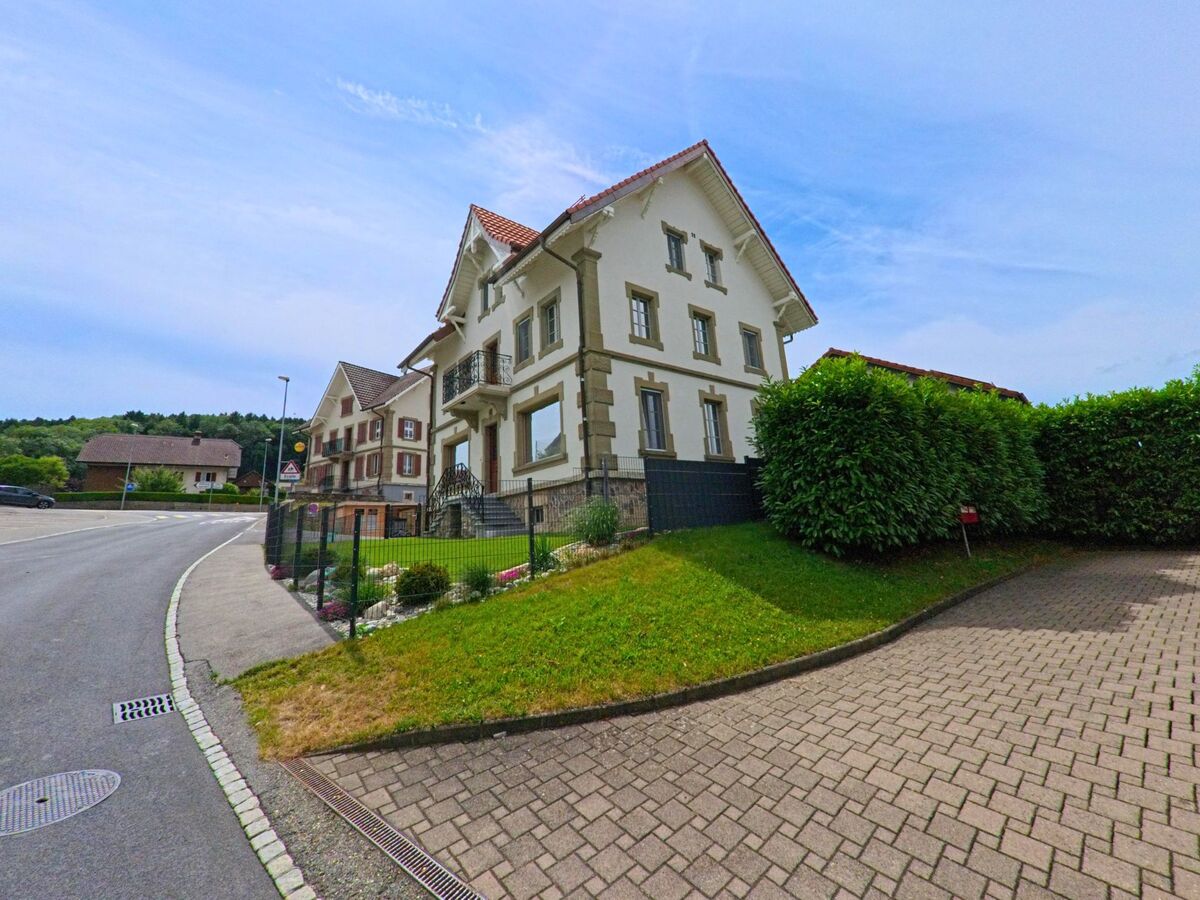 In Bois-d’Amont (1732, Kanton Freiburg) stehen mehrere stilvolle Wohnhäuser mit gepflegten Vorgärten entlang einer sanft geschwungenen Strasse.