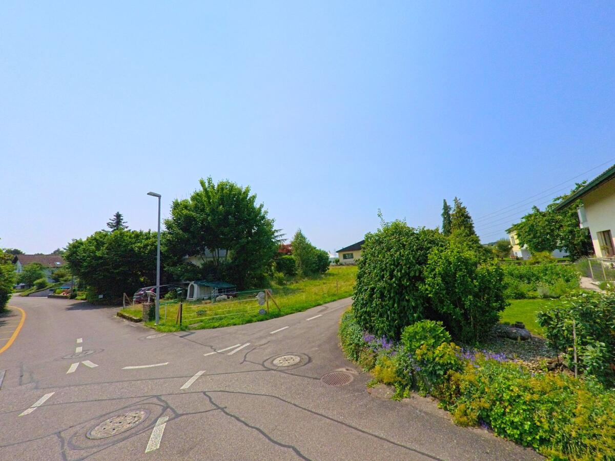 In Bolken (4556, Kanton Solothurn) zweigt ein schmaler Weg zwischen Gaerten und Wohnhaeusern von einer Quartierstrasse ab, begleitet von dichter Vegetation.
