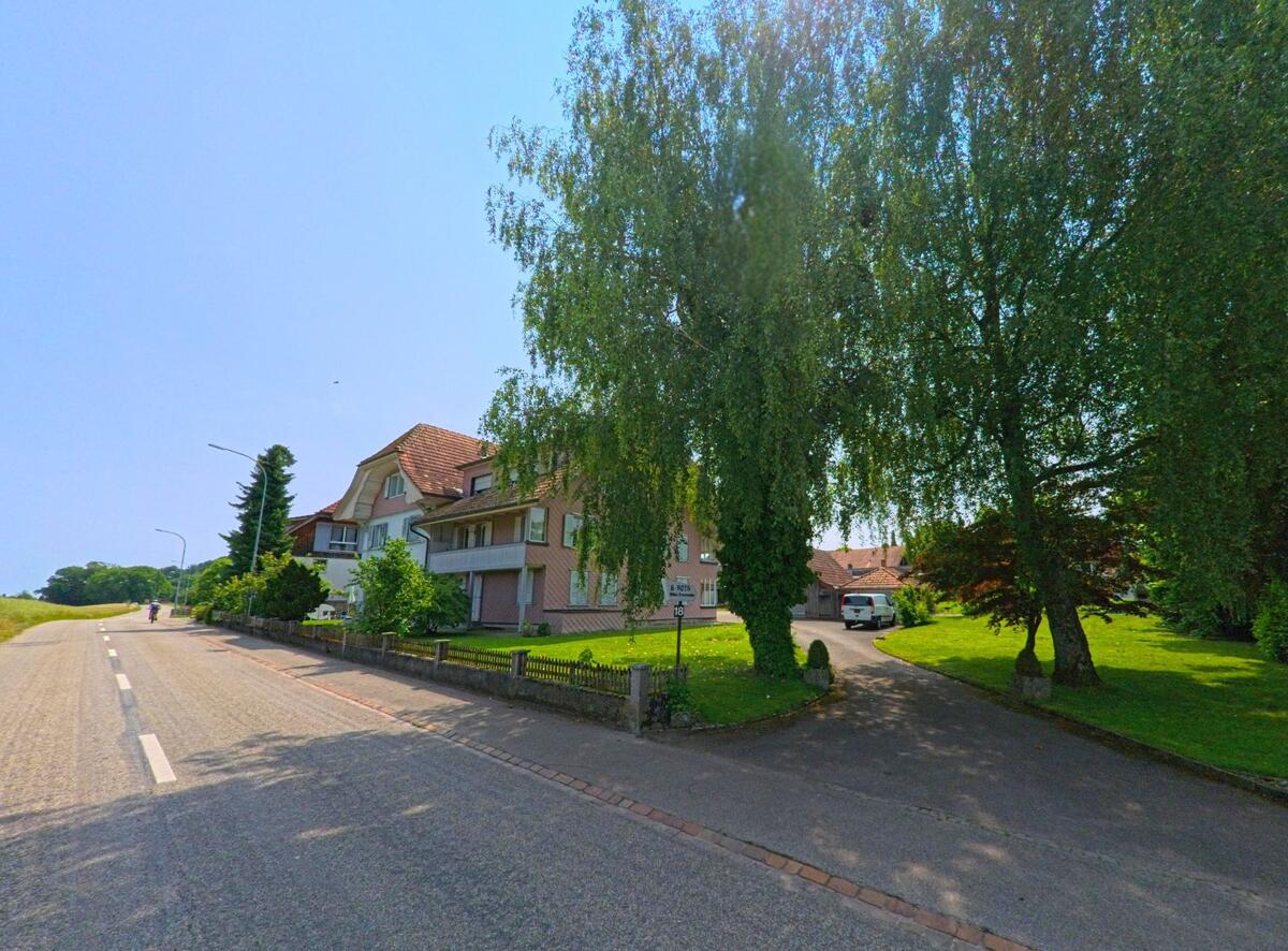 Ein grosses Wohnhaus in Bolken (4556, Kanton Solothurn) liegt an einer leicht ansteigenden Strasse, umgeben von grossen Baeumen und gruener Rasenflaeche.