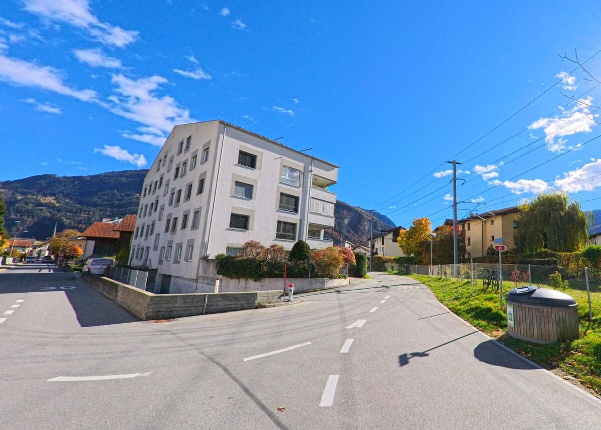 An einer abzweigenden Strasse in Bonaduz (7402, Kanton Graubünden) steht ein mehrstöckiges Wohngebäude neben einer ruhigen Seitenroute mit Blick auf die umliegenden Berge.