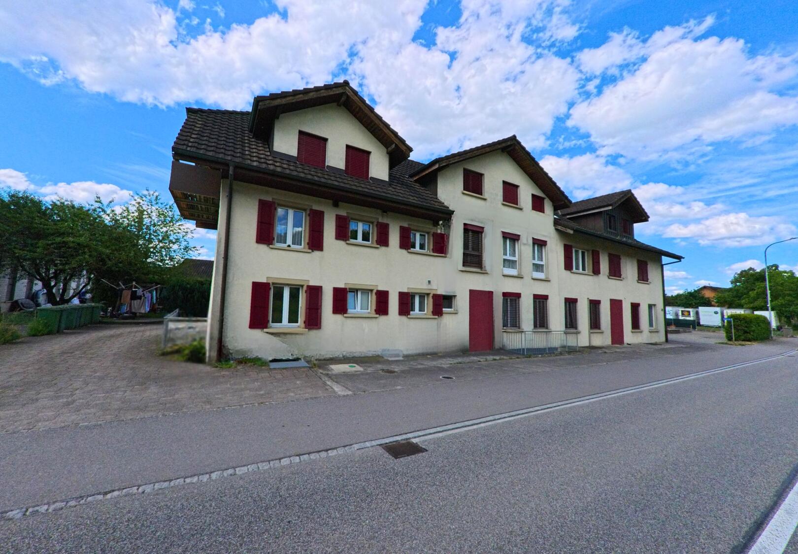 An einer Hauptstrasse in Boningen (PLZ 4618, Kanton Solothurn) steht ein mehrstöckiges Wohnhaus mit roten Fensterläden und mehreren Eingängen.