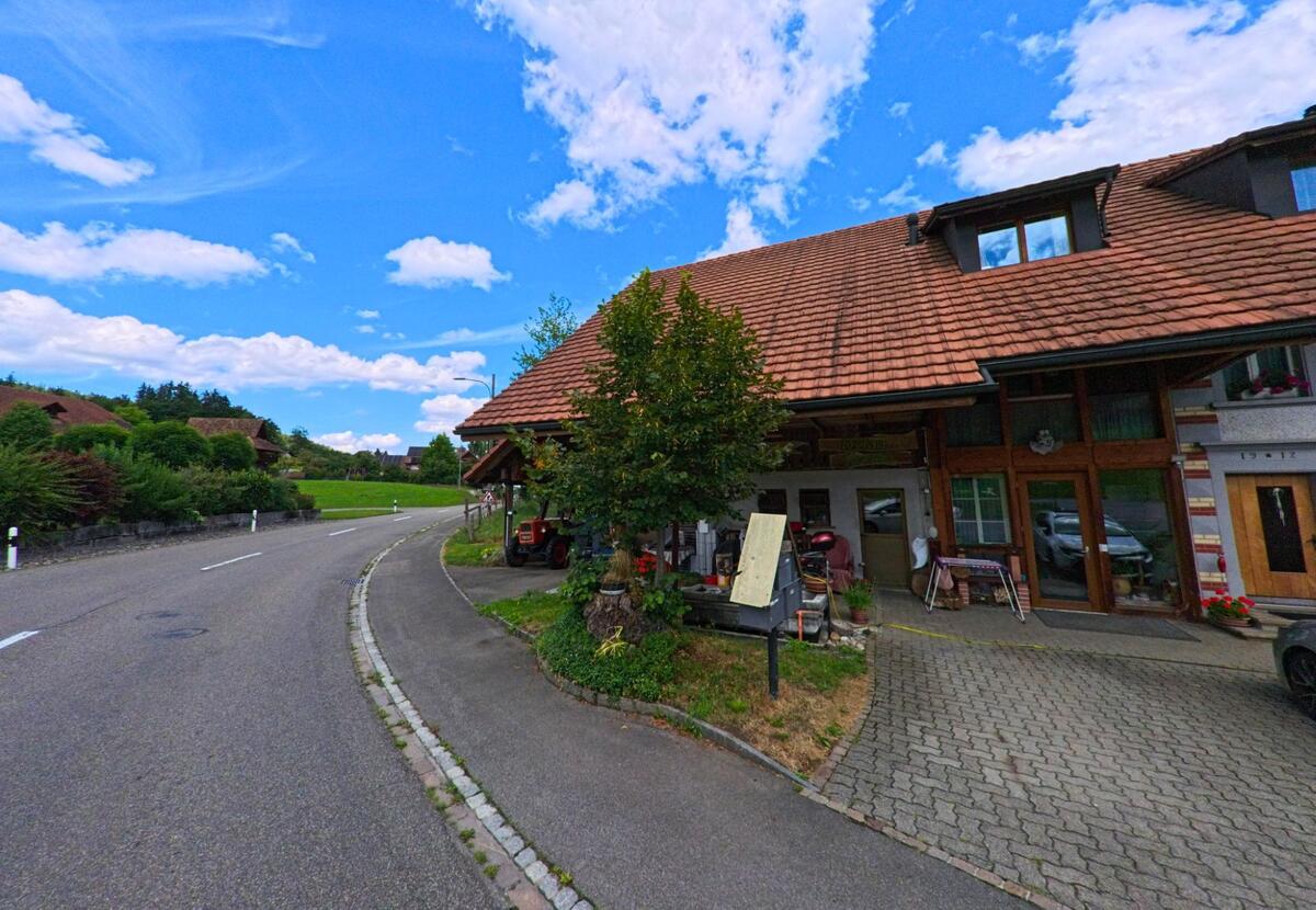 In Bottenwil (4814, Kanton Aargau) liegt ein Bauernhaus mit Verkaufsstand direkt an einer leicht geschwungenen Landstrasse, vor dem ein kleiner Traktor geparkt ist.