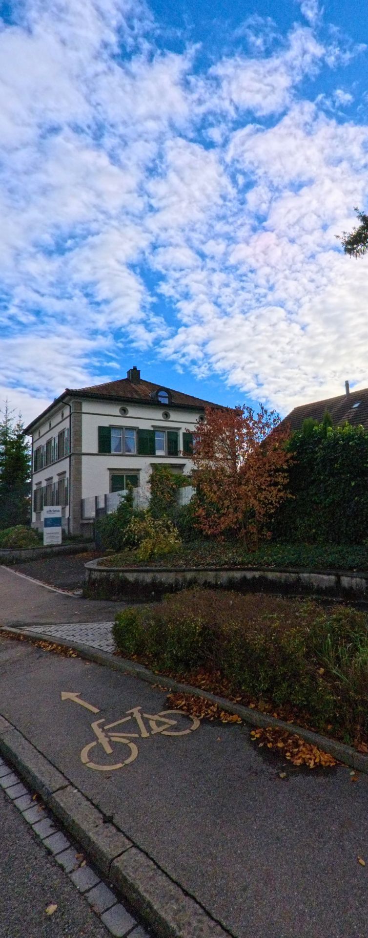 Ein markierter Veloweg fuehrt an einem Wohngebaeude mit Garten vorbei und praegt das ruhige Umfeld in Bottighofen (8598, Kanton Thurgau) unter herbstlichem Himmel.