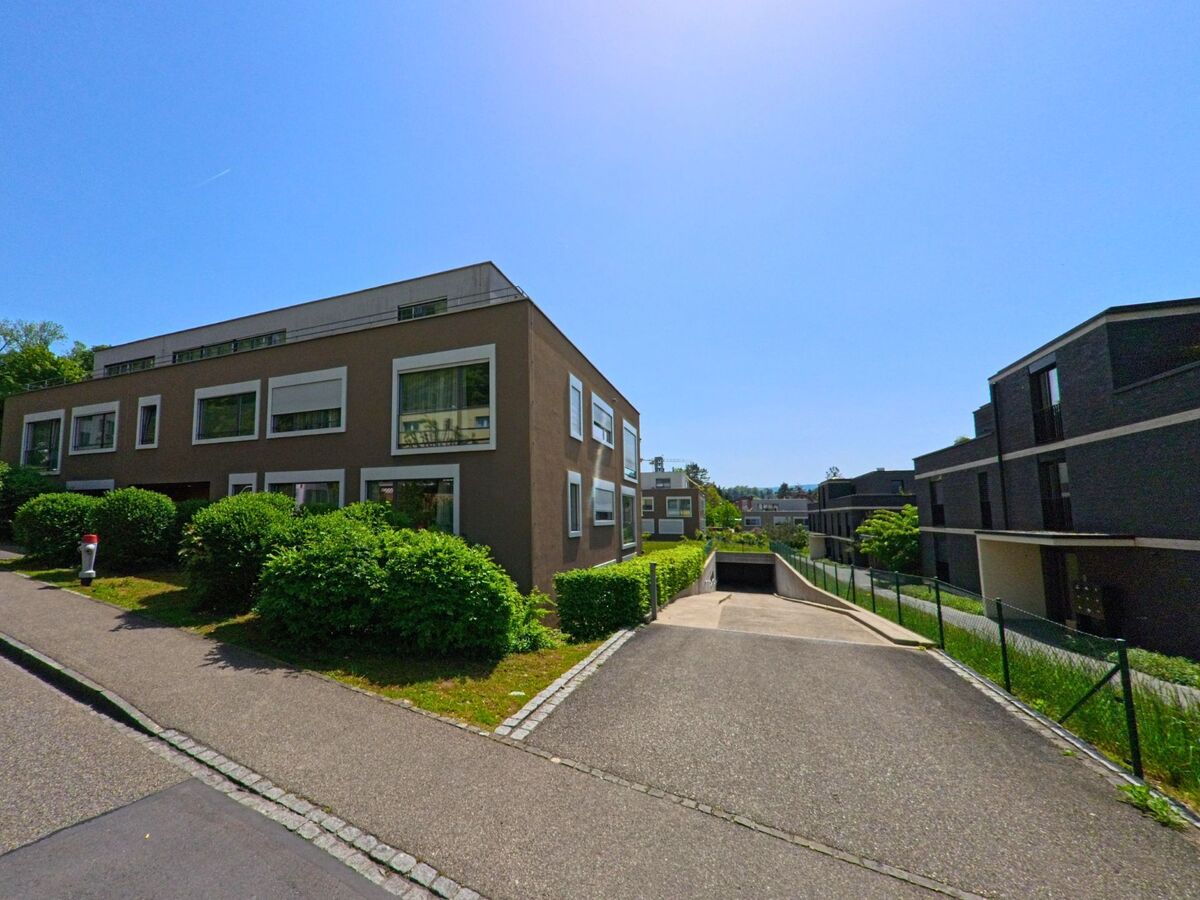 In Bottmingen (4103, Kanton Basel-Landschaft) liegen moderne Wohnhäuser mit grossen Fenstern entlang eines Zugangs zur Tiefgarage, umgeben von gepflegten Hecken.