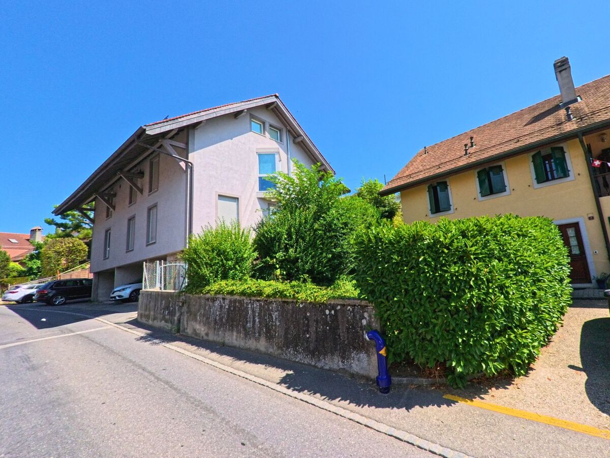 Zwei angrenzende Wohnhaeuser mit unterschiedlichen Fassadenfarben und Gaerten befinden sich in einer ruhigen Strasse von Bournens (1035, Kanton Waadt).