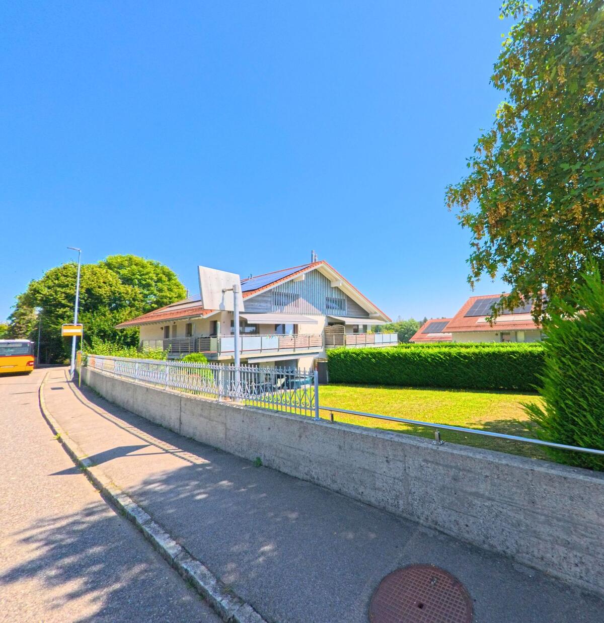 Ein modernes Wohnhaus mit Balkonen und Garten liegt in Boussens (1034, Kanton Waadt) an einer Strasse mit Bushaltestelle.