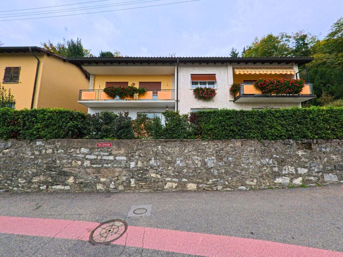 Ein Wohnhaus an der Via Cantonale in Breggia (6835, Kanton Tessin) zeigt helle Fassaden mit Blumenkästen an den Balkonen und einer niedrigen Steinmauer davor.