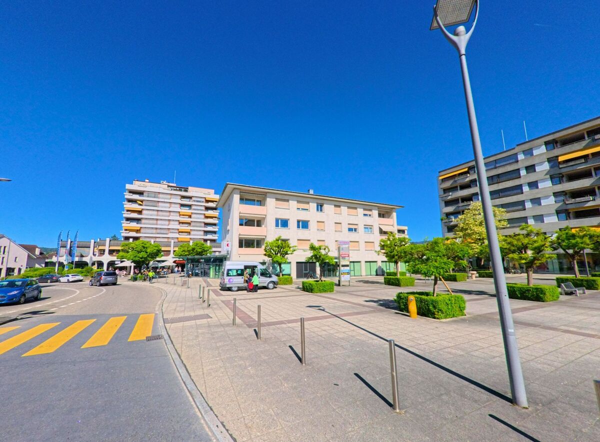  In Breitenbach (4226, Kanton Solothurn) oeffnet sich ein moderner Platz mit Sitzgelegenheiten, flankiert von Geschaeftsgebaeuden und Wohnanlagen.