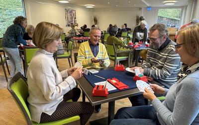 Im Bridge Club Luzern in Luzern (6005, Kanton Luzern) spielen mehrere Personen konzentriert eine Runde Bridge in einem hellen Raum mit weiteren Tischen im Hintergrund.