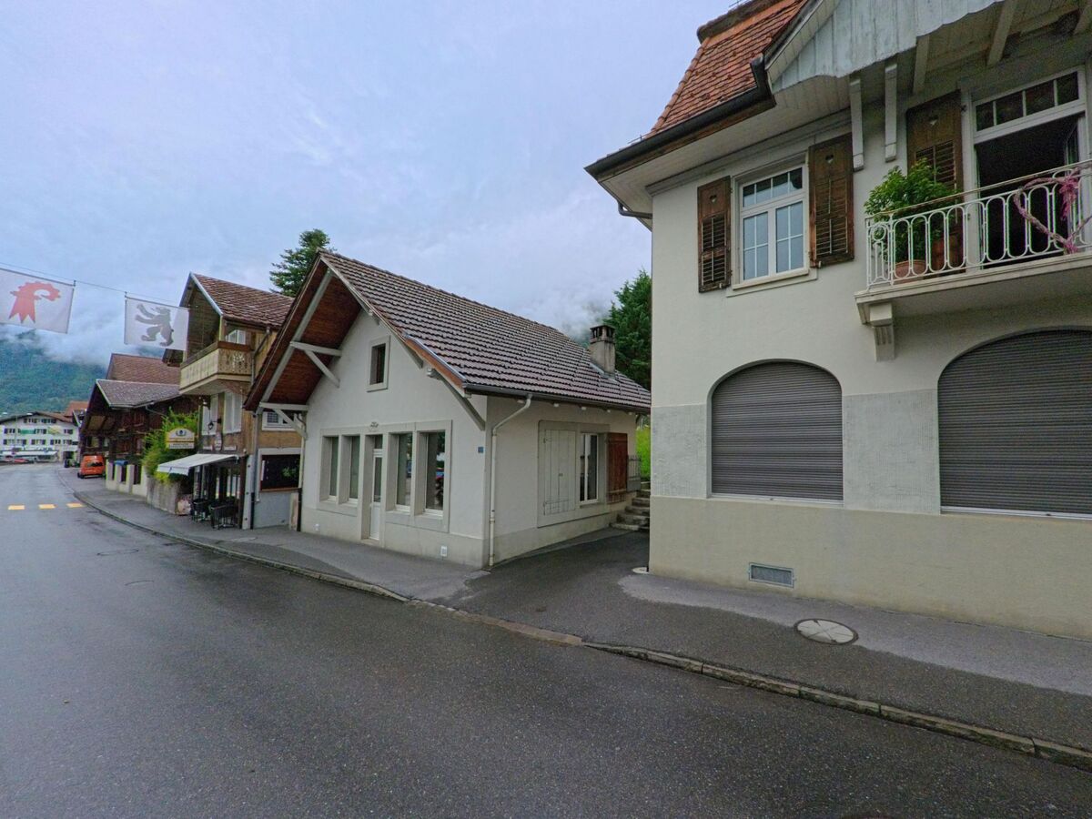 In Brienz (3855, Kanton Bern) säumen kleine Ladengebäude und Wohnhäuser mit Holzbalkonen eine zentrale Strasse, über der Gemeindefahnen hängen.