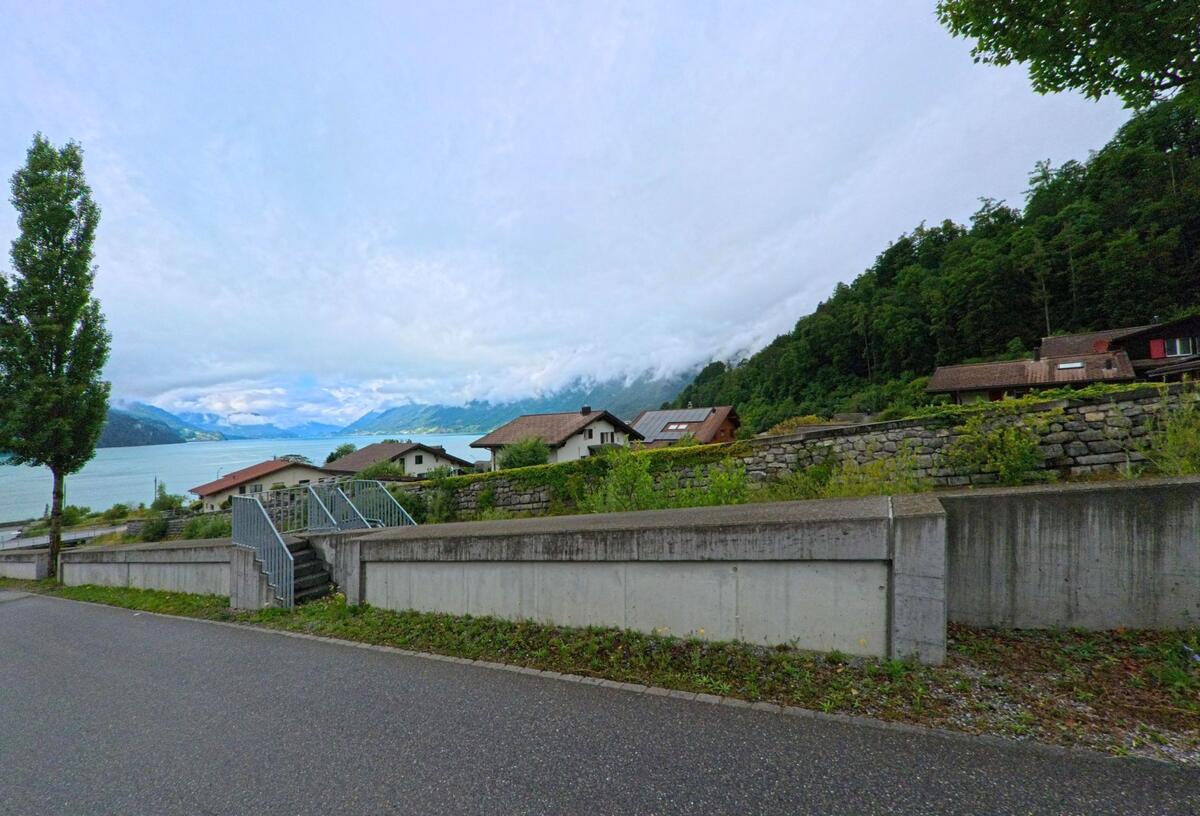 In Brienz (3855, Kanton Bern) führt eine Treppe über eine niedrige Mauer zu einer Siedlung mit Blick auf den Brienzersee und die umliegenden Berge.