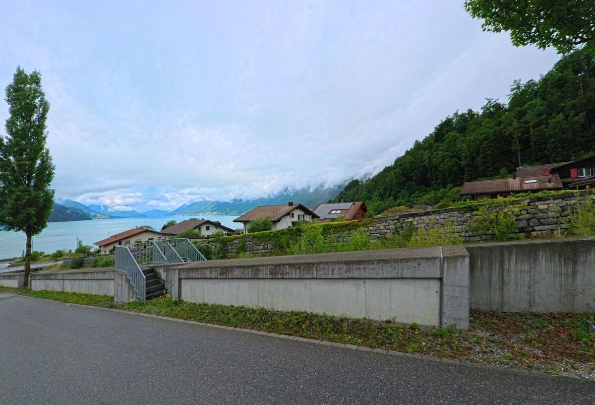 In Brienz (3855, Kanton Bern) führt eine Treppe über eine niedrige Mauer zu einer Siedlung mit Blick auf den Brienzersee und die umliegenden Berge.