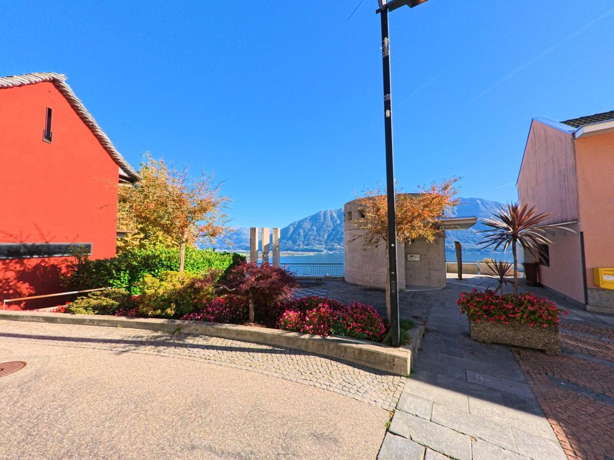Zwischen bunten Häusern in Brione sopra Minusio (6645, Kanton Tessin) liegt ein kleiner Platz mit Blumenbeeten und Blick auf den Lago Maggiore.