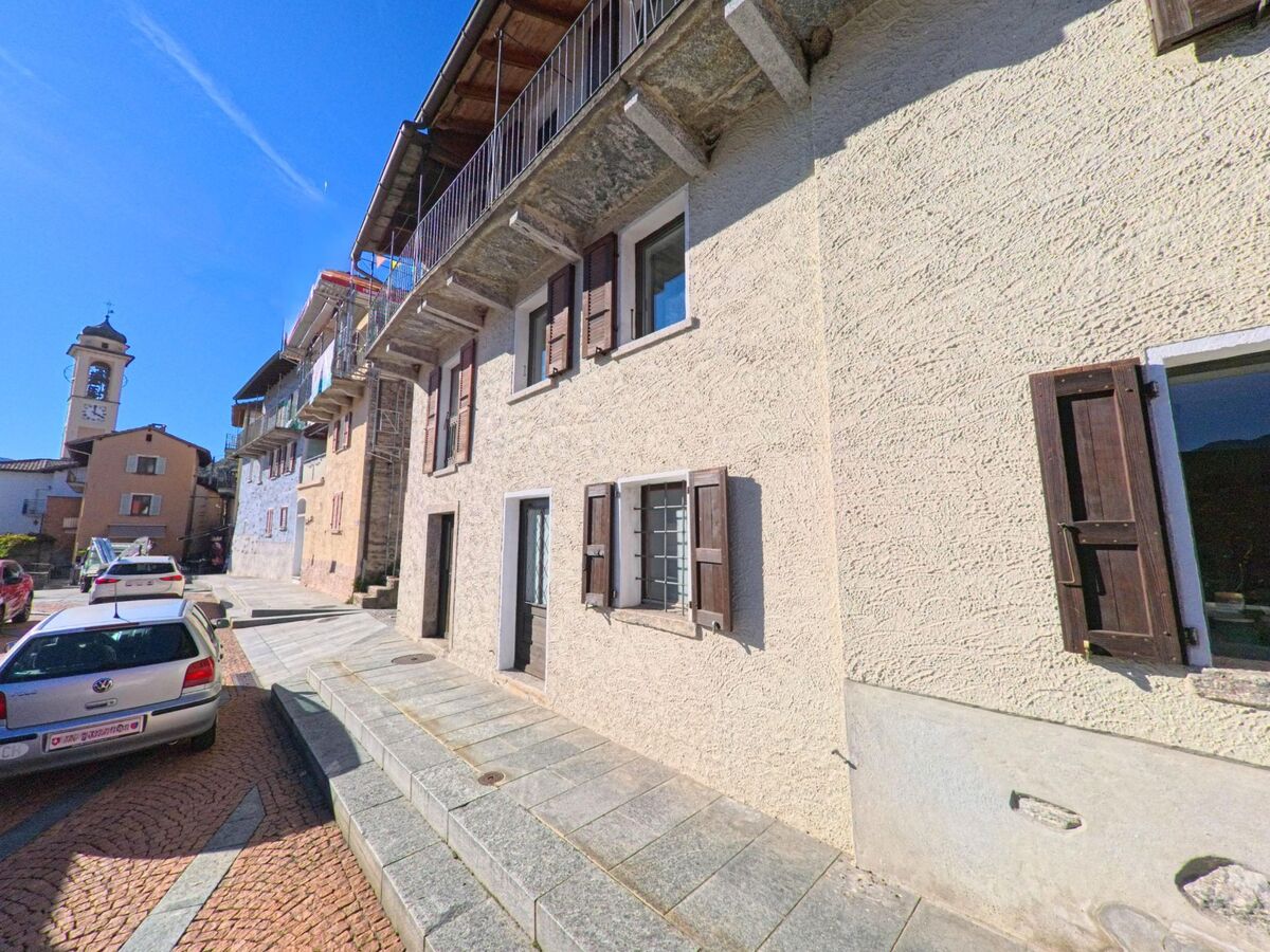 In der Hauptgasse von Brione sopra Minusio (6645, Kanton Tessin) stehen Häuser mit Fensterläden, im Hintergrund der Kirchturm des Dorfes.