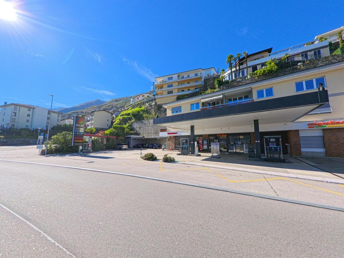 In Brissago (6614, Kanton Tessin) liegt eine Tankstelle mit Laden an der Hauptstrasse, umgeben von terrassierten Häusern am Berghang.